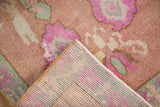 Distressed pile of a vintage Oushak rug showing pink and green floral details and hand-knotted reverse.