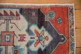 Distressed Oushak rug corner detail: rust field, charcoal spandrel, with turquoise pinwheel motifs.
