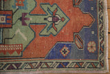Distressed vintage Oushak rug corner showing border and spandrel in terracotta, royal blue, and green.