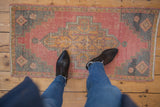 Distressed Oushak rug corner with stepped motif, abrashed coral and charcoal tones.