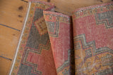 Folded distressed Oushak rug runner with worn texture, coral, gray, and gold geometric motifs.