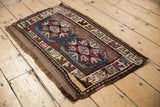 Vintage distressed Kars rug corner with geometric arrowed border in plum and pale blue.