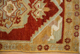 Distressed Oushak rug corner, showing worn cherry red pile and intricate beige, green motifs.