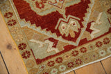 Distressed Oushak rug corner, showing worn cherry red and sand serpent-like arabesques.