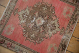 Distressed pink Oushak rug corner, showing floral spandrel and visible knot heads.