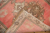 Folded distressed Oushak rug, revealing pink pile with faint foundation and beige reverse.