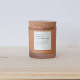 Warm orange Sweet Clementine Soy Candle in frosted glass with a cork lid.