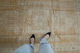 Distressed vintage Oushak rug showing soft gold and antique ivory geometric patterns.