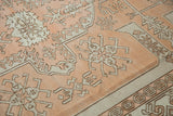 Distressed Oushak rug close-up: geometric vines, soft pile texture, and patterned border.