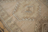 Distressed beige Oushak rug with geometric medallion, sand tones, and visible wear.