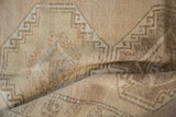 Textured folds of a distressed Oushak rug runner, showing beige and pale brown geometric motifs.