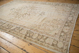 Distressed Turkish Oushak carpet corner, showing worn ivory pile and muted vine motifs.