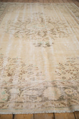 Distressed vintage Oushak carpet's worn ivory pile with faint foundation and fringe.