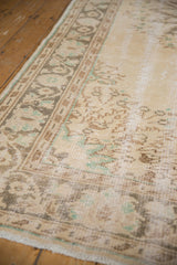 Distressed Oushak carpet border and field, showcasing faded ivory, brown, and muted green motifs with wear.