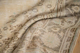 Distressed vintage Oushak carpet pile showing textured wear and muted ivory-brown patterns.