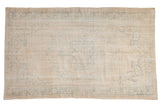 Vintage distressed Oushak carpet with an ivory field and faded Rococo-inspired curvilinear patterns.