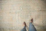 Close-up of distressed Oushak rug: ivory field, faded teal curvilinear pattern, mostly even wear.
