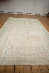 Vintage distressed Oushak carpet with worn ivory pile and subtle faded blue-green motifs.