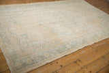 Detail of distressed Oushak rug corner with worn ivory pile and faded teal patterns.