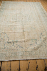 Distressed vintage Oushak carpet showing worn ivory pile with faint blue-green patterns.