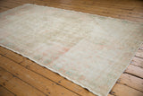 Distressed Oushak rug showing exposed foundation, wear across knot heads, and pale blush and turquoise.