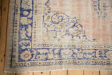 Distressed vintage Oushak rug corner; pale rose field, cobalt blue border, knot heads, and fringe.
