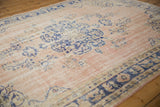 Faint cobalt blue floral motifs on a distressed dusty rose Oushak rug, showing foundation.