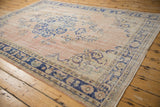 Distressed Oushak rug corner with mostly even wear, pale rose field, and blue floral border.