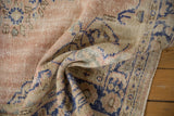 Distressed Oushak rug texture in dusty rose, ivory, and cobalt blue with fringed edge.