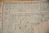 Distressed vintage Oushak corner, soft beige and pale green vine patterns.