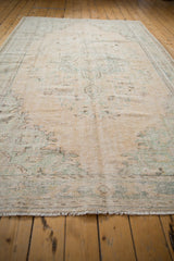 Faded aqua floral motifs on the distressed beige field of a vintage Oushak rug.