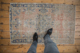 Overhead personal view of a small distressed Oushak rug showing its faded rose and blue floral pattern for scale.