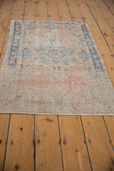 Decorative vintage Oushak rug with a distressed rose and blue pattern, shown on an angle.