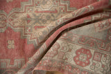 Distressed Oushak rug pile in soft folds, showing pale red, silver, and ivory geometric patterns.