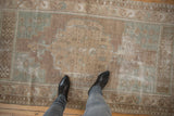 Person's boots on a vintage distressed Oushak rug, highlighting worn texture and muted colors.