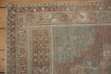 Worn beige, brown, and seafoam green patterns on a distressed vintage Oushak rug corner.
