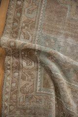 Distressed vintage Oushak rug texture with faded beige, green, and brown floral patterns.