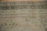 Distressed pile of vintage Oushak rug showing geometric patterns in ivory, charcoal, and pink.