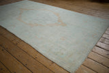 Angled perspective of a distressed Oushak rug showing its full length and soft, faded pile.