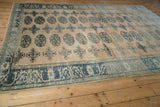 Distressed Oushak rug section featuring geometric guls, sand field, and an ornate blue border.