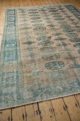 Distressed vintage Oushak rug with faded geometric gul motifs and intact side selvage.