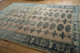 Distressed Oushak rug corner with charcoal border, pale floral motifs, and worn texture.