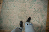 Vintage distressed Oushak rug, showcasing faded seafoam geometric patterns and textural wear.