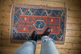 Distressed vintage Melas rug featuring geometric cranberry red, indigo blue, and ivory patterns.