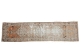 Distressed vintage Oushak runner with faded tangerine, terracotta, and blue stepped diamond medallions.