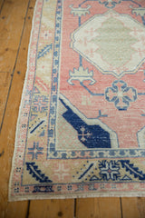 Distressed Oushak runner corner with dusty rose, cobalt blue geometric patterns, intact selvage.