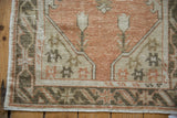 Terracotta, ivory, and charcoal vintage Oushak rug corner, showing distressed pile with stylized patterns.