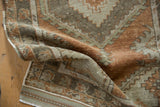 Corner view of distressed Oushak rug, showing worn pile, secured selvage, and fringe.