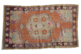 Distressed Oushak rug with terracotta field, scalloped floral medallion, purple and pink accents.