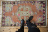 Distressed terracotta Oushak rug with pink floral medallion and purple starburst border.